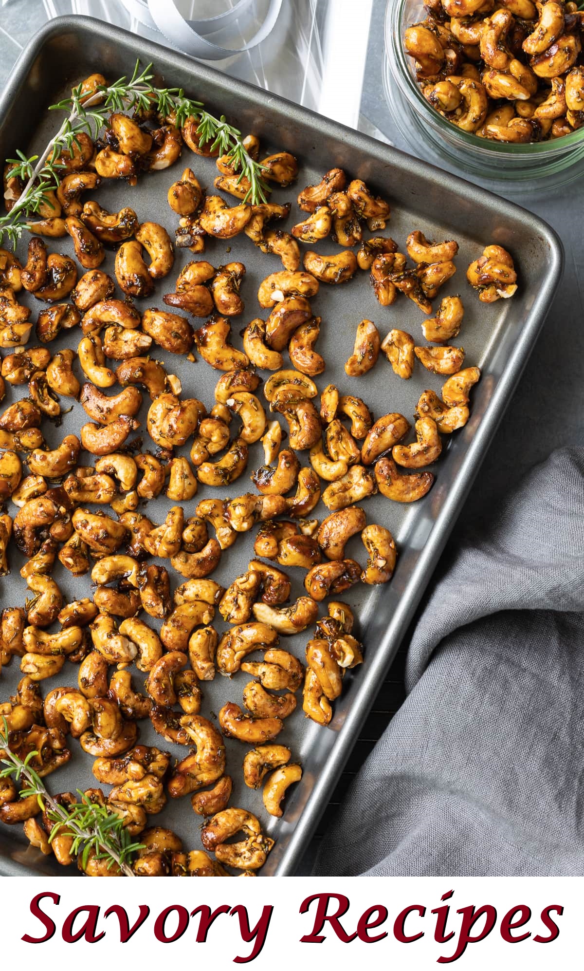 Freshly roasted maple-glazed cashews spread on a warm baking tray with rosemary.